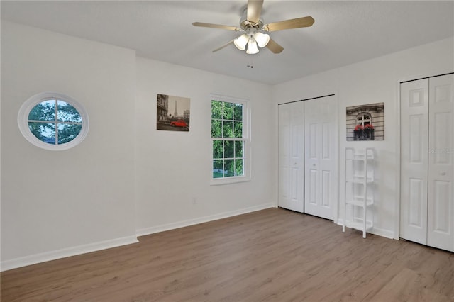 unfurnished bedroom featuring light wood-type flooring, ceiling fan, and multiple closets