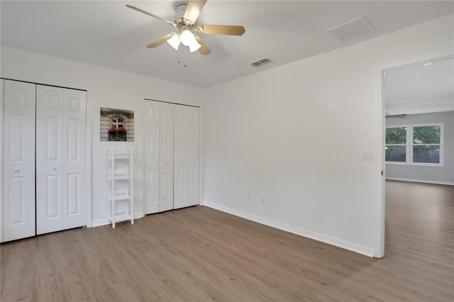 unfurnished bedroom featuring ceiling fan, light hardwood / wood-style flooring, and multiple closets