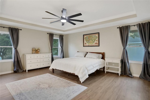 bedroom featuring multiple windows, a raised ceiling, hardwood / wood-style floors, and ceiling fan