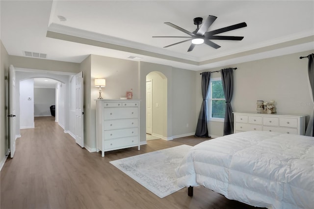 bedroom featuring ceiling fan, ornamental molding, a tray ceiling, and light hardwood / wood-style floors