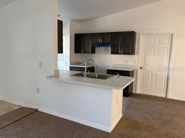 kitchen featuring kitchen peninsula, sink, vaulted ceiling, and dark colored carpet