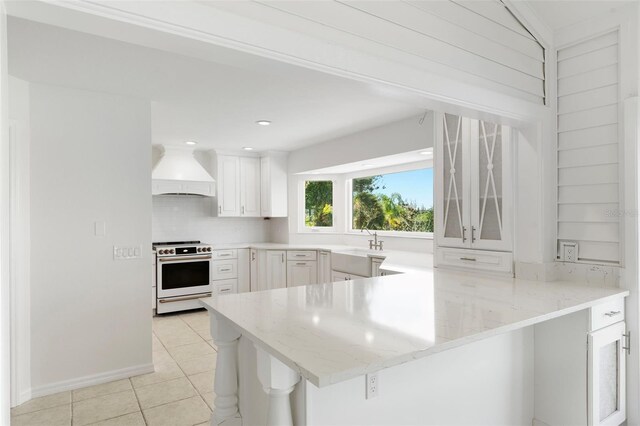 kitchen with white cabinets, stove, custom range hood, and kitchen peninsula