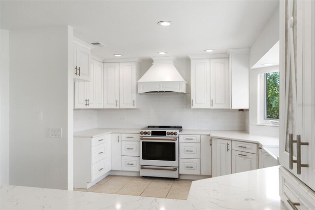 kitchen featuring decorative backsplash, stove, custom exhaust hood, and white cabinets