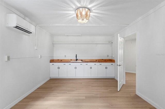 kitchen with white cabinets, light hardwood / wood-style flooring, sink, and a wall mounted AC