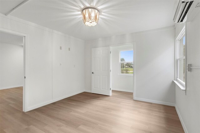 unfurnished room with crown molding, light hardwood / wood-style floors, a wall mounted AC, and a notable chandelier