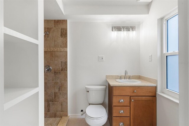 bathroom with tile patterned flooring, tiled shower, vanity, and toilet