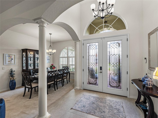 tiled entrance foyer featuring decorative columns, a towering ceiling, french doors, and a notable chandelier