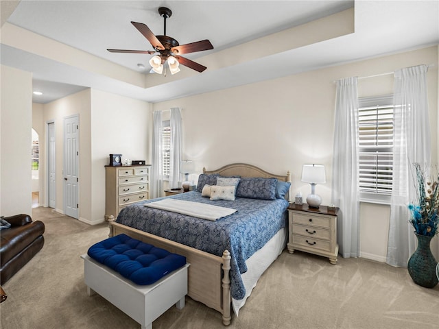 bedroom featuring a raised ceiling, ceiling fan, and light colored carpet