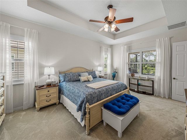 bedroom with a tray ceiling, light carpet, and ceiling fan