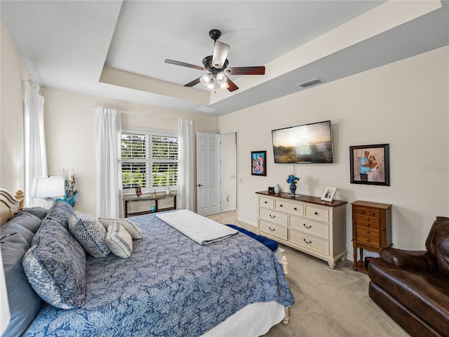 bedroom featuring ceiling fan, a tray ceiling, and light carpet