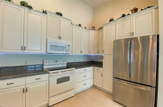 kitchen with dark stone countertops, white appliances, light tile patterned floors, and white cabinets