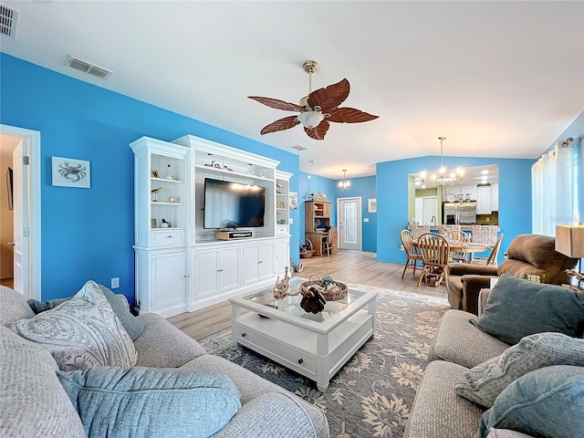 living room with ceiling fan with notable chandelier, light wood-type flooring, and lofted ceiling