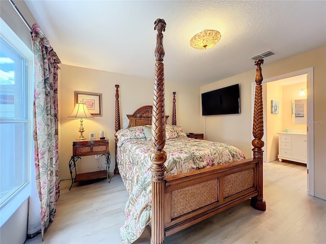 bedroom with a textured ceiling, ensuite bath, and light hardwood / wood-style floors