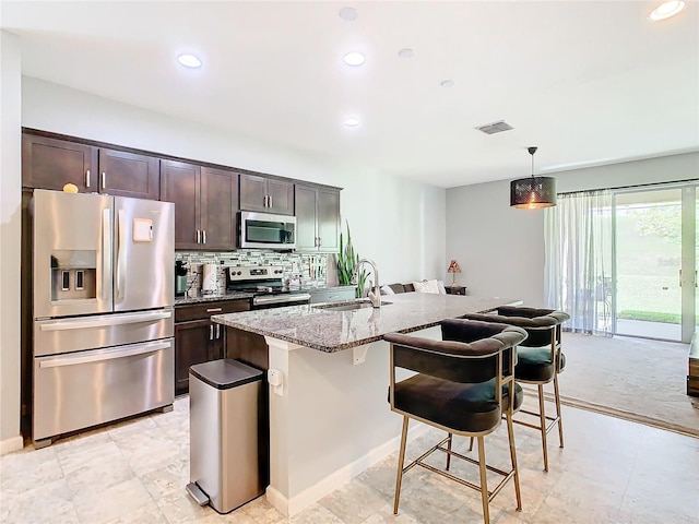 kitchen with hanging light fixtures, an island with sink, light stone counters, stainless steel appliances, and sink