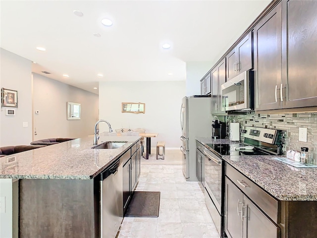 kitchen featuring light stone counters, an island with sink, sink, stainless steel appliances, and decorative backsplash