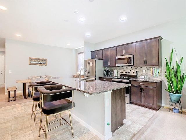 kitchen featuring sink, a center island with sink, appliances with stainless steel finishes, a breakfast bar, and light stone countertops