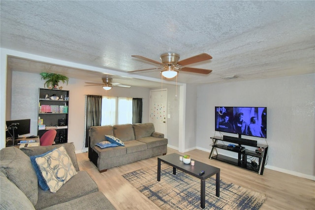 living room with ceiling fan, a textured ceiling, and light wood-type flooring