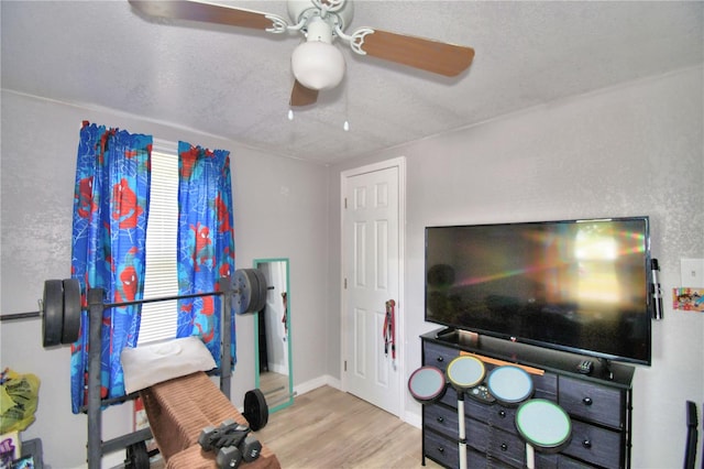 exercise room featuring light wood-type flooring, a textured ceiling, and ceiling fan