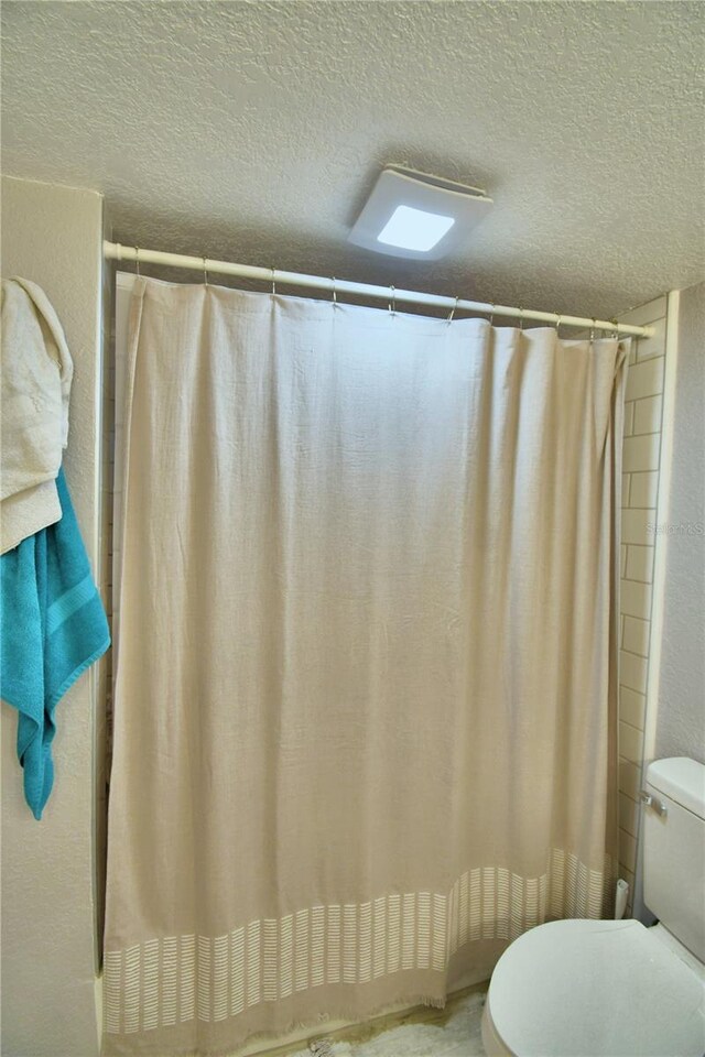 bathroom featuring a textured ceiling, toilet, and a shower with shower curtain