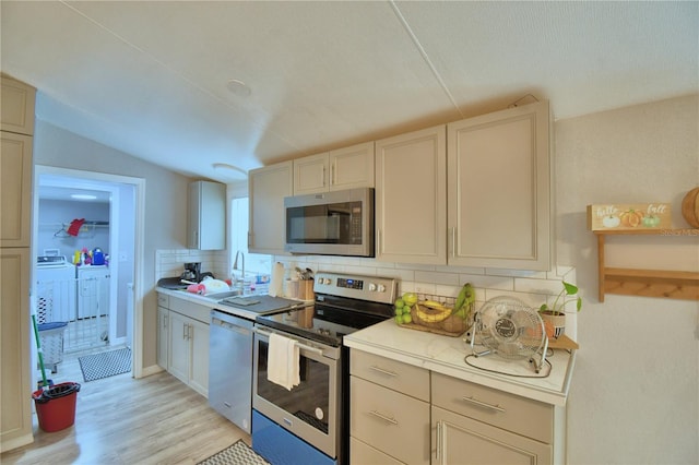 kitchen with appliances with stainless steel finishes, decorative backsplash, washer and dryer, and light hardwood / wood-style flooring