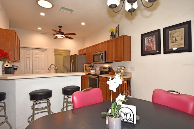 kitchen with sink, ceiling fan with notable chandelier, kitchen peninsula, a kitchen breakfast bar, and stainless steel appliances