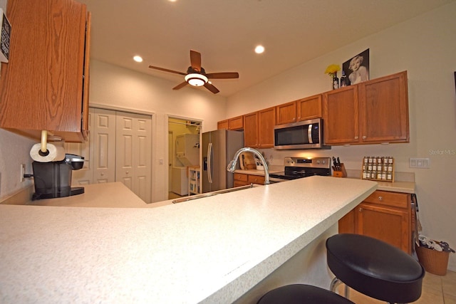 kitchen with a kitchen breakfast bar, light tile patterned flooring, stainless steel appliances, ceiling fan, and sink