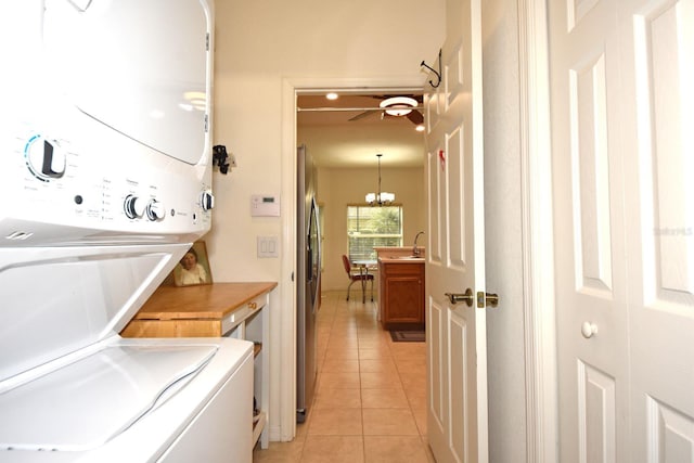 laundry room with sink, ceiling fan with notable chandelier, stacked washer / dryer, and light tile patterned floors