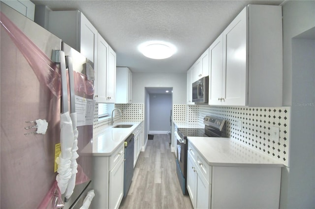 kitchen with light wood-type flooring, sink, white cabinets, backsplash, and appliances with stainless steel finishes