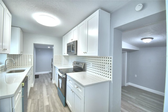 kitchen featuring light wood-type flooring, sink, white cabinetry, decorative backsplash, and appliances with stainless steel finishes