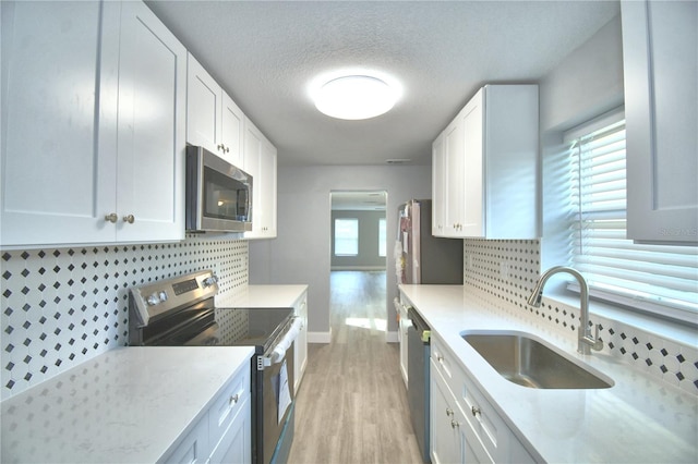 kitchen featuring sink, backsplash, white cabinetry, stainless steel appliances, and light hardwood / wood-style floors