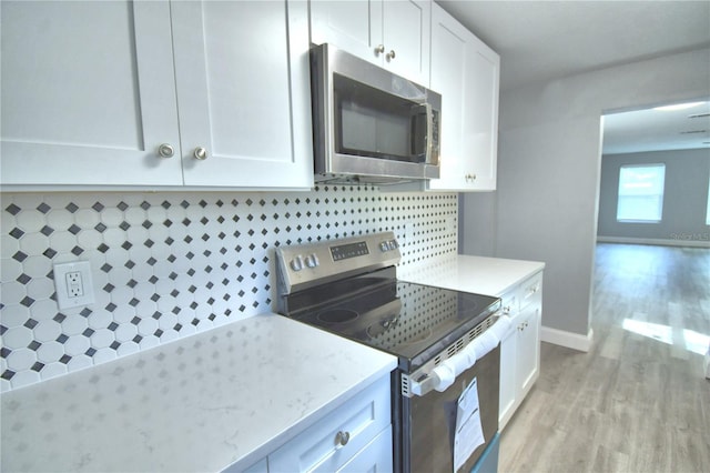 kitchen featuring light stone counters, white cabinetry, appliances with stainless steel finishes, light wood-type flooring, and decorative backsplash