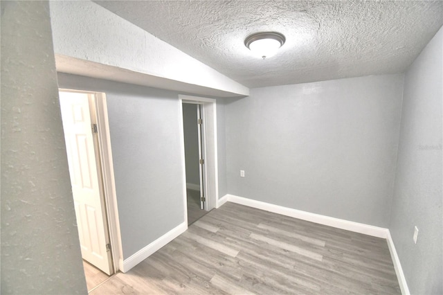 spare room with a textured ceiling, wood-type flooring, and vaulted ceiling