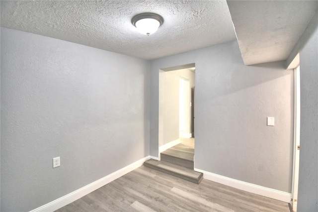 empty room with a textured ceiling and light hardwood / wood-style flooring