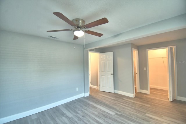 unfurnished bedroom with light hardwood / wood-style flooring, a closet, ceiling fan, and a walk in closet