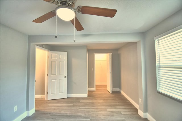 unfurnished bedroom featuring light hardwood / wood-style floors, a spacious closet, ceiling fan, and a closet