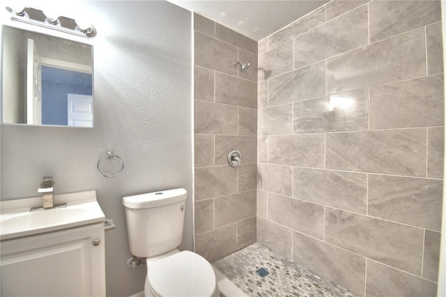 bathroom featuring a tile shower, vanity, and toilet