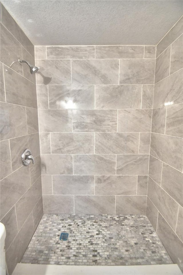 bathroom with a textured ceiling and tiled shower