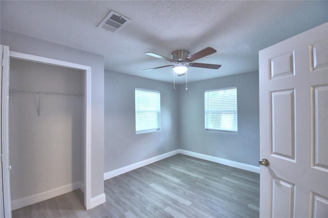 unfurnished bedroom with a textured ceiling, ceiling fan, a closet, and hardwood / wood-style flooring