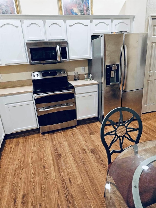 kitchen with stainless steel appliances, white cabinetry, and light wood-type flooring