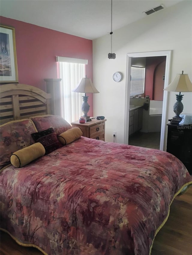 bedroom featuring vaulted ceiling, wood finished floors, visible vents, and ensuite bathroom