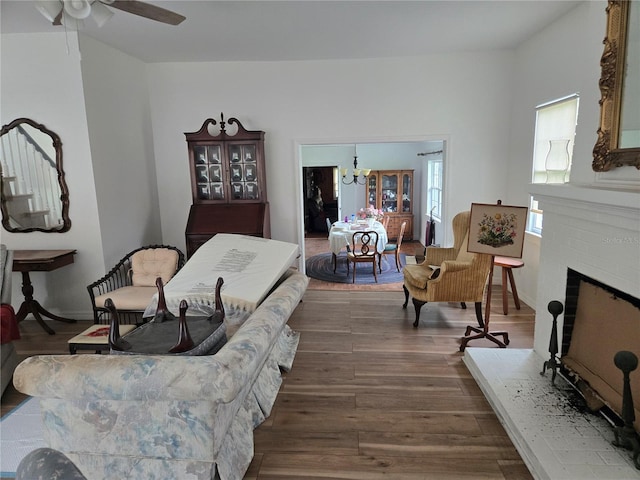 living room with ceiling fan with notable chandelier, a brick fireplace, and dark hardwood / wood-style flooring