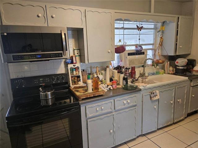 kitchen featuring sink, light tile patterned floors, black range with electric stovetop, and white cabinets