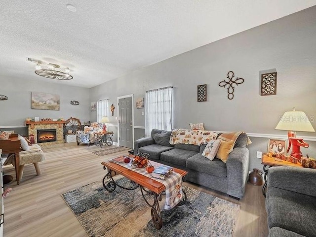 living room featuring a textured ceiling, wood-type flooring, and a stone fireplace