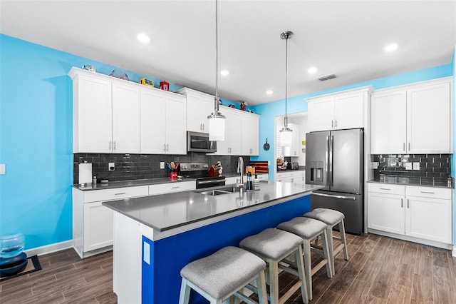 kitchen with appliances with stainless steel finishes, hanging light fixtures, white cabinetry, and dark hardwood / wood-style floors