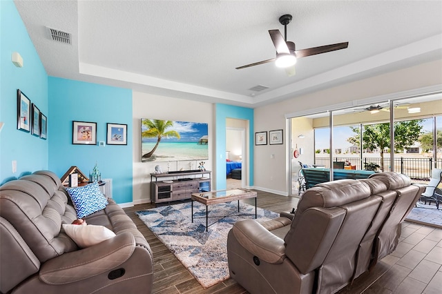 living room with ceiling fan, dark wood-type flooring, a raised ceiling, and a textured ceiling