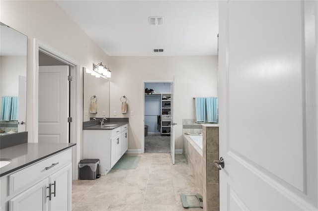 bathroom with tiled tub, vanity, and tile patterned floors