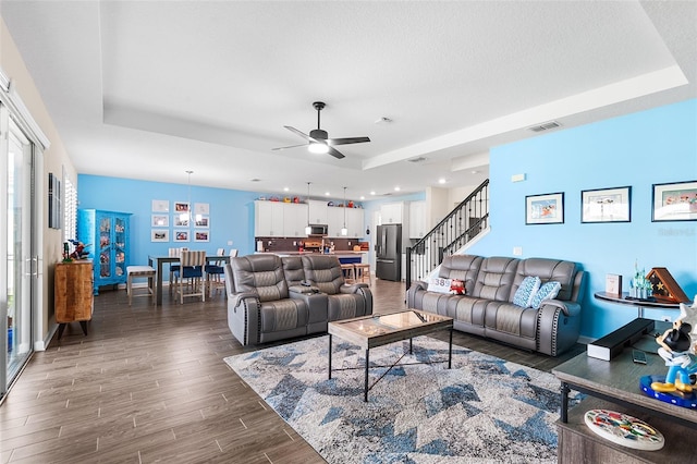 living room featuring ceiling fan, a tray ceiling, and dark hardwood / wood-style floors