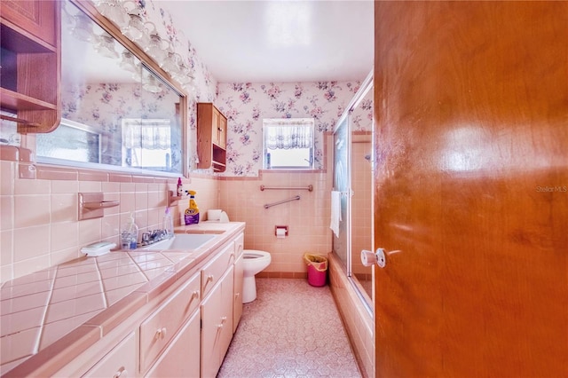 full bathroom with a wealth of natural light, bath / shower combo with glass door, vanity, tile patterned flooring, and toilet