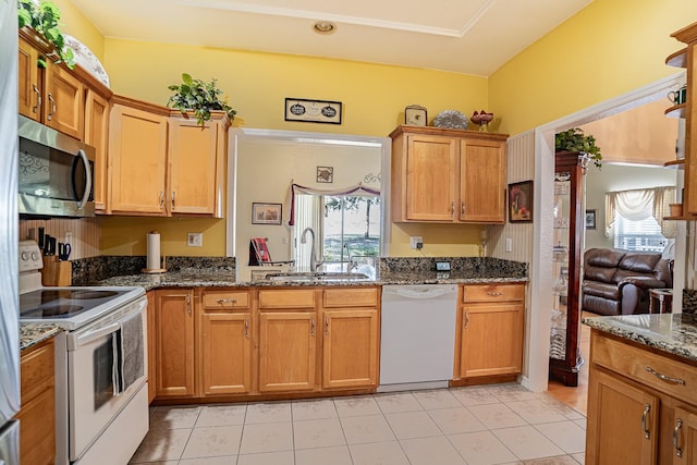 kitchen with white appliances, dark stone countertops, sink, and light tile patterned floors