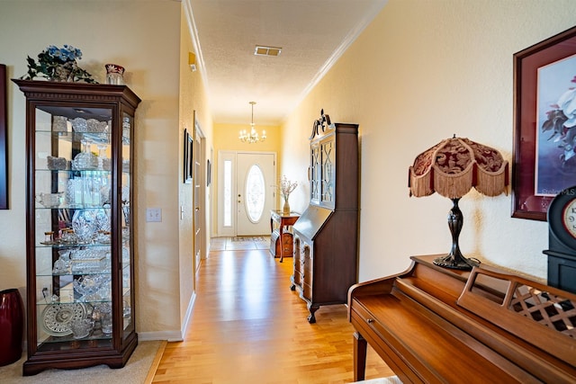 entrance foyer with a textured ceiling, light wood-type flooring, crown molding, and a chandelier